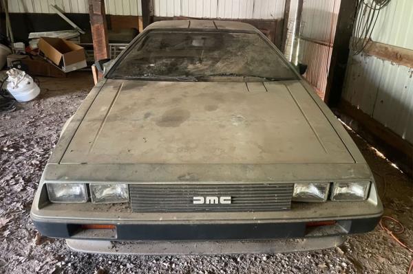 A 1981 DeLorean parked in a barn and covered with dust.