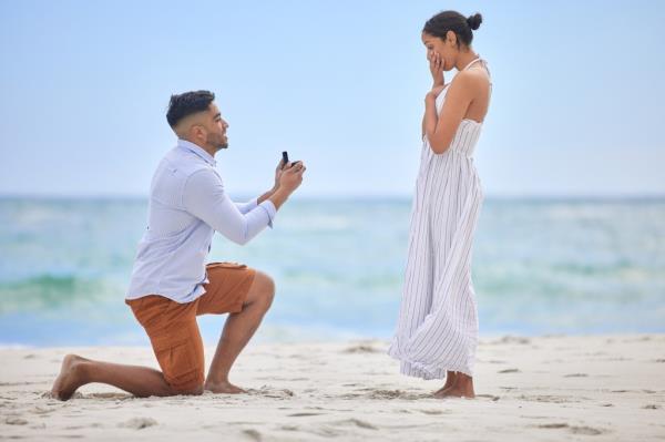 Young man proposing to his girlfriend on a beach during summertime