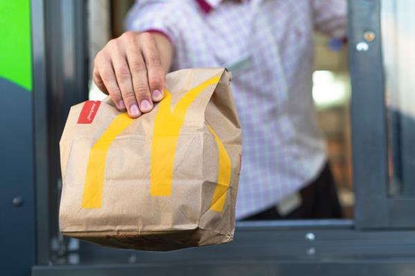 McDonald's worker holding bag of fast-food out drive-thru window.