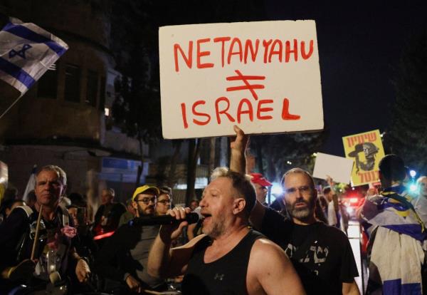 Man holding a sign and singing into a microphone during a protest against Israeli Prime Minister Benjamin Netanyahu near his residence in Jerusalem