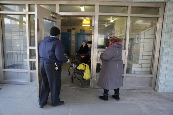 A security guard helps a woman through the door at a Brooklyn NYCHA facility.