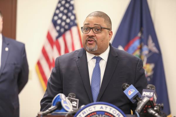 Man in suit & tie speaking into microphones.