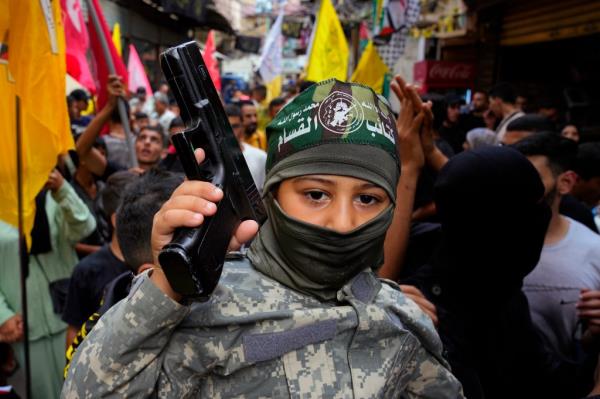 A Palestinian boy wearing army-style fatigues holds a gun as others dance in celebration of the attacks that the militant Hamas group carried out against Israel.