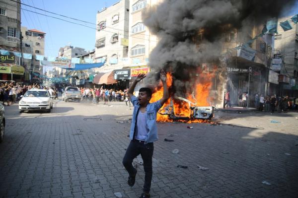 A Palestinian man celebrates by a burning Israeli civilian car taken from Kfra Azza kibbutz in Beit Lahiya.