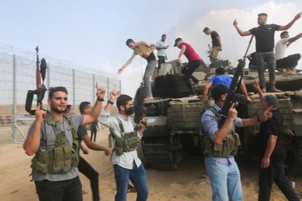 Palestinian militants celebrate by an Israeli tank at the border fence of the Gaza Strip following Hamas' attack on the Jewish nation on October 7.