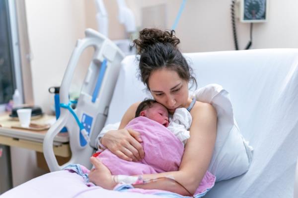 A beautiful and relaxed ethnic mother is snuggling her newborn and affectio<em></em>nately holding her in the hospital after delivery.