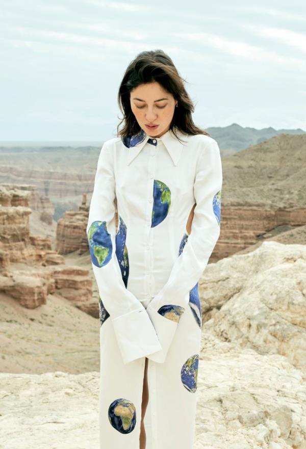 A photo of Rosas wearing a white dress with images of the earth on it, standing near an unnamed canyon.
