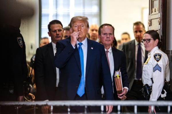 Former president Do<em></em>nald Trump leaves the courtroom and signals to the press that under oath he is not able to speak during his court trial