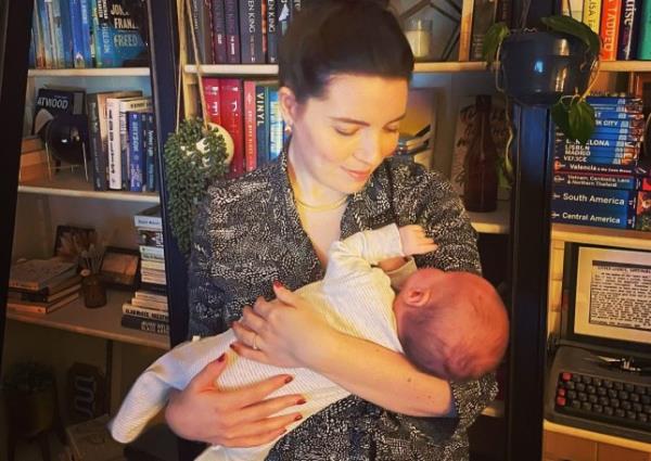 Siobhan Smith at home, holding her baby, with bookshelves behind her.