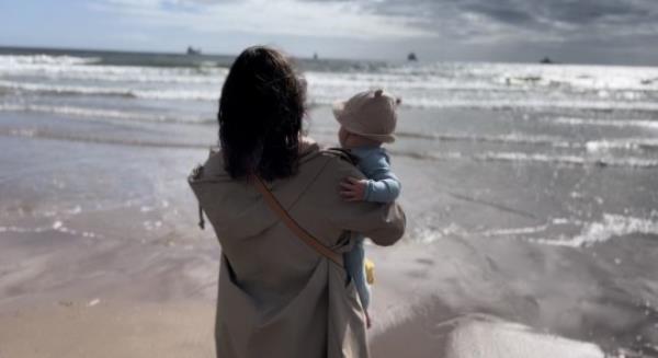 Siobhan Smith holding her baby on a beach, both of them looking out to sea, their backs to the camera.