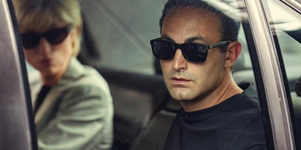 Elizabeth Debicki, Khalid Abdalla as Diana and Dodi, wearing sunglasses sitting in a car. 