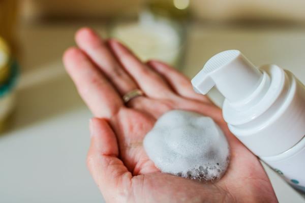 Man looking in the mirror while washing face with soap and exfoliation mask as part of his morning skincare routine