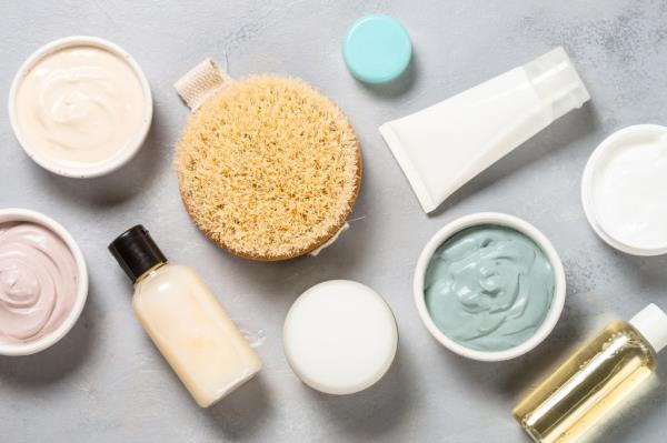 Top view of a variety of natural skincare products including a clay mask, cream, shower gel, sponge, and cosmetic oil on a pink background.