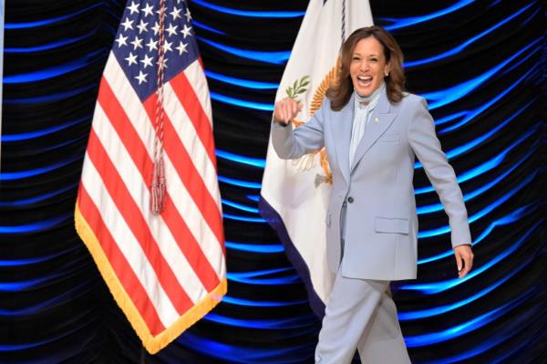 harris in a light blue pant suit smiling and walking out on a stage with a blue background and an american flag</p>

<p>　　