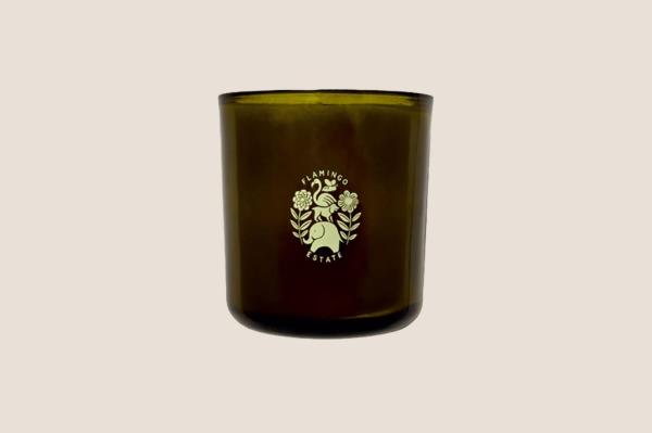 A green candle holder with a white logo and Climbing Tuscan Rosemary Candle label