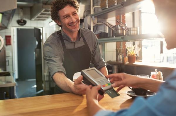 Woman paying by credit card and entering pin code on reader holded by smiling barista in cafeteria