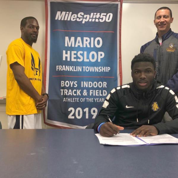 Mario Heslop sits in front of a banner announcing his win of MileSplit 