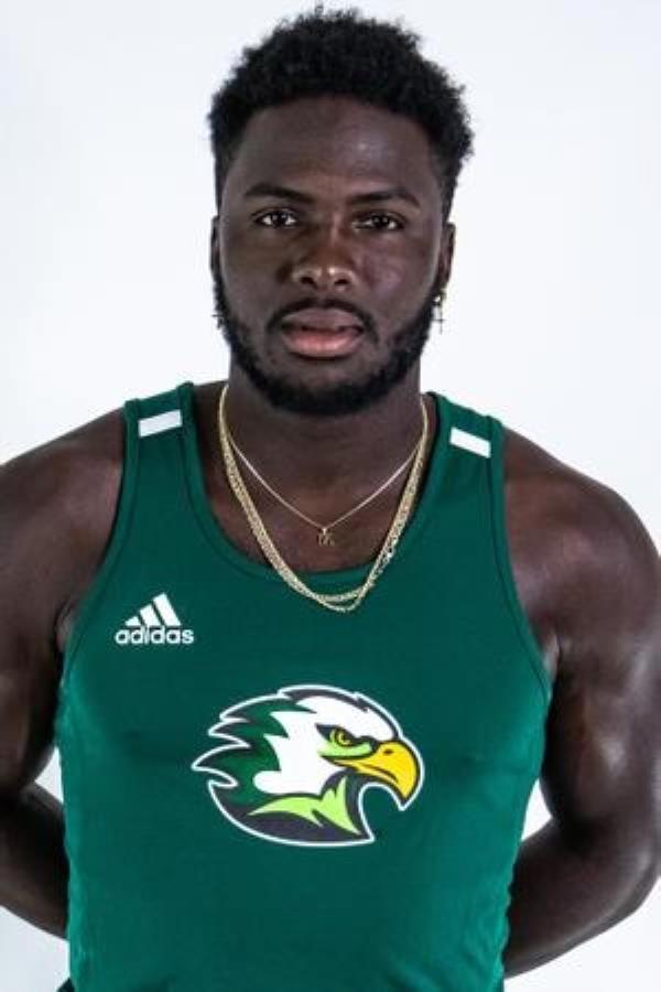 Mario Heslop poses with in his hands behind his back wearing a green track tank with an eagle on it. 