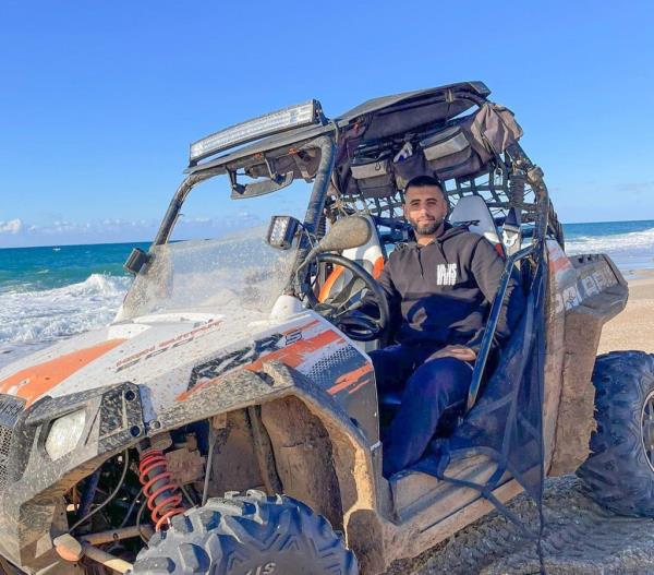 Raz Peri driving an ATV on a beach, with waves in the background.