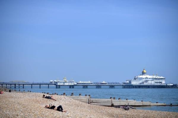 Sun seekers lie on a near-deserted beach near the pier in Eastbourne, southern England on May 9, 2020, as life in Britain co<em></em>ntinues over the May bank holiday weekend, during the natio<em></em>nwide lockdown due to the novel coro<em></em>navirus COVID-19 pandemic. - The British government warned the public on Friday not to expect any major changes to the natio<em></em>nwide coro<em></em>navirus lockdown next week, as the official daily death toll topped 31,000. (Photo by Ben STANSALL / AFP) (Photo by BEN STANSALL/AFP via Getty Images)