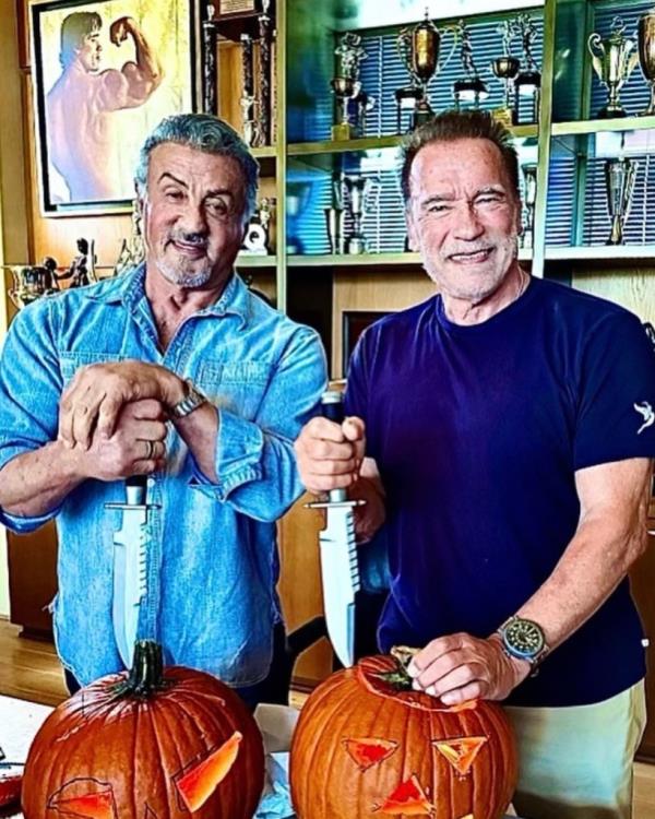 Arnold Schwarzenegger and Sylvester Stallone carve pumpkins.
