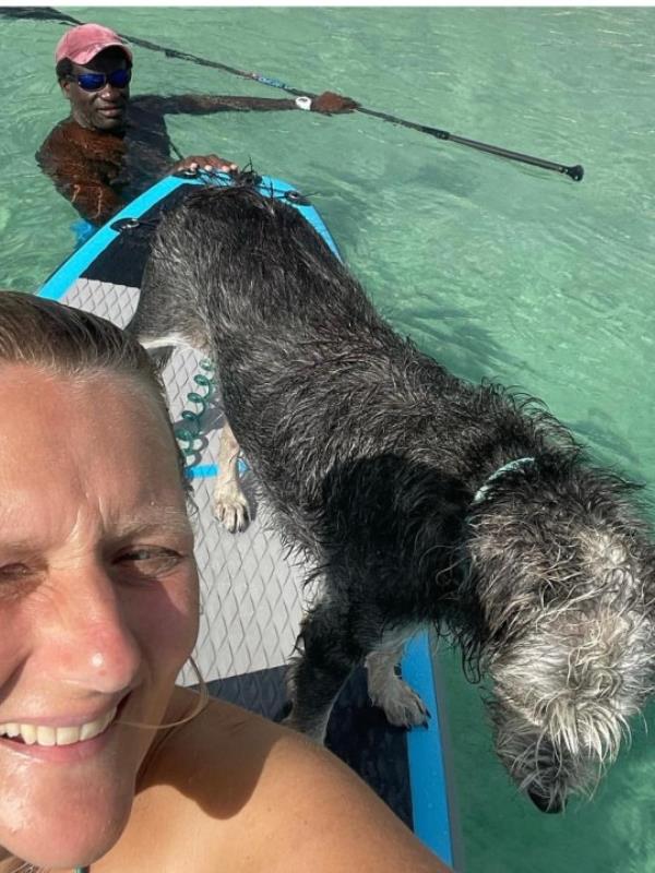 a woman paddle boarding with her husband and dog. 