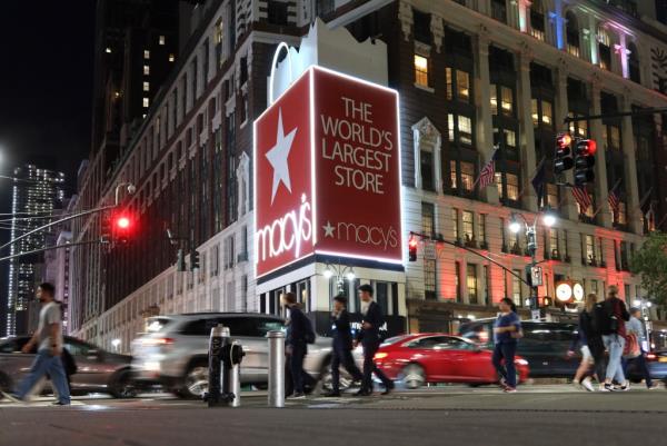People walking past a large Macy's billboard on a building in New York City