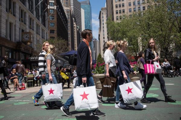Shoppers carrying bags walking through Herald Square outside Macy's on 34th Street in New York City, indicating a rise in co<em></em>nsumer spending
