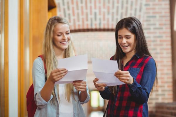 Two smiling students opening college acceptance letters