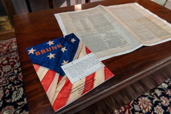 An auction booklet next to a facemile of a signed official ratification copy of the United States Co<em></em>nstitution by Brunk Auction.
