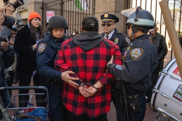 A male pro-Palestine protester is in handcuffed and flanked by two cops.