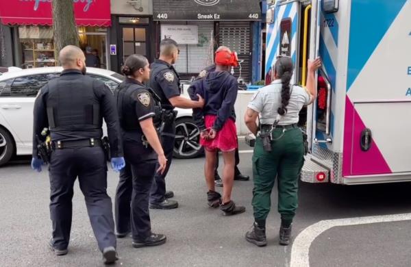 Police officers walk a woman wearing handcuffs into the back of an ambulance. 