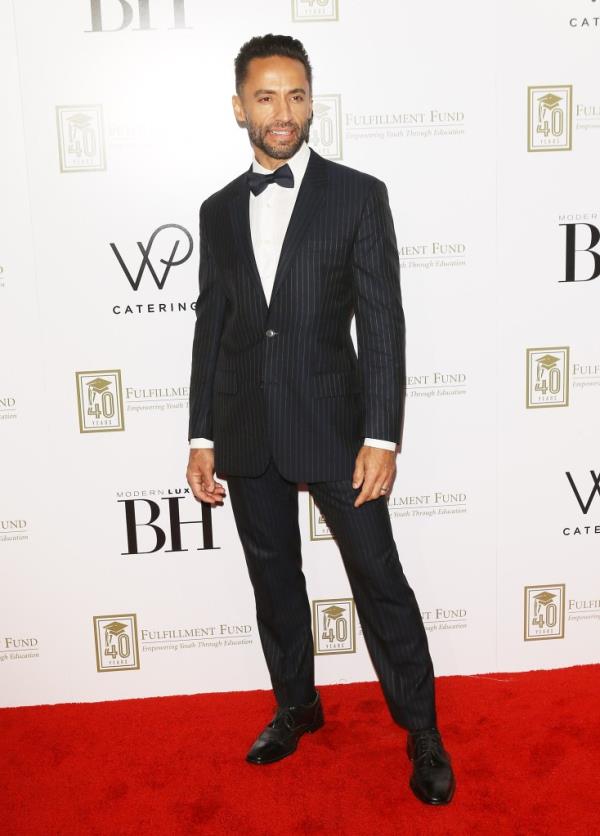 Kamar de los Reyes  smiling in a suit. 