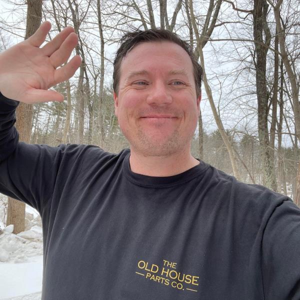 A man in a long-sleeve t-shirt is seen waving in front of the woods