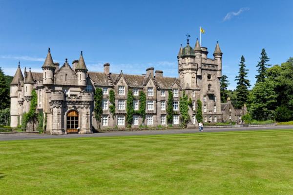 Balmoral Castle, the summer residence of the British Royal Family, a large stone baro<em></em>nial revival style building with towers and a well-maintained lawn in Aberdeenshire, Scotland.