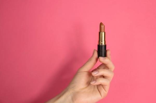 hand holding up a brown lipstick against a pink background