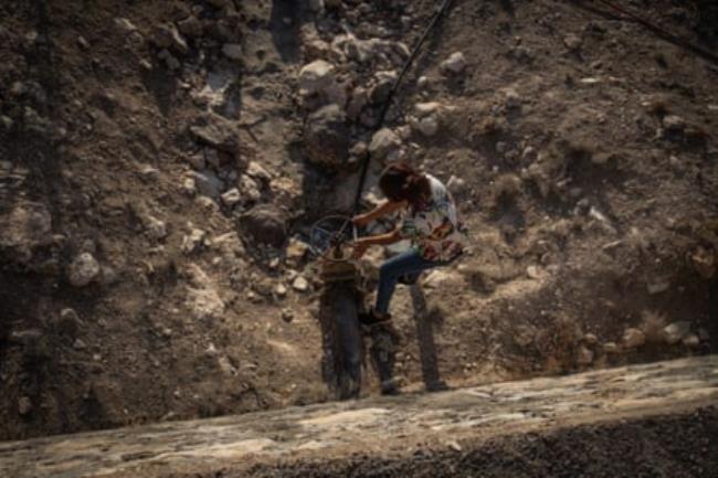 A woman kneels in the dust to turn a wheel co<em></em>nnected to a water pipe