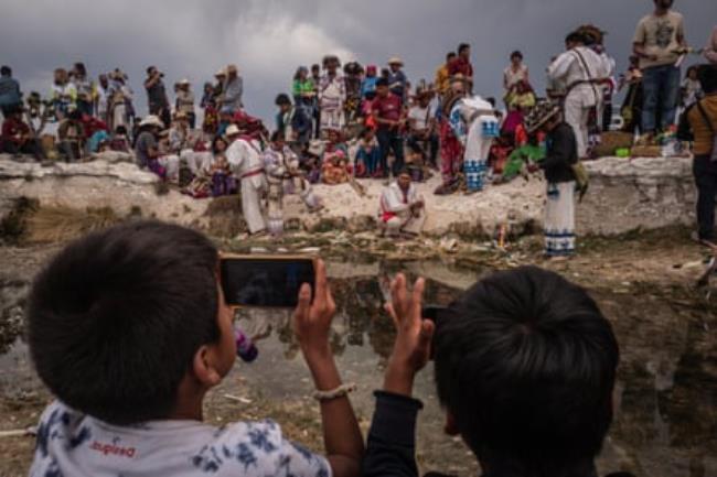 Two children photograph a procession on Wixárika pilgrims