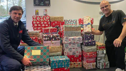 BBC Maksym Litvinov and Andy Evangelou crouch next to a pile of Christmas presents. 