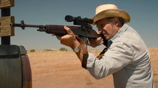 Liam Neeson standing with a rifle pointed at something, in the desert in The Marksman